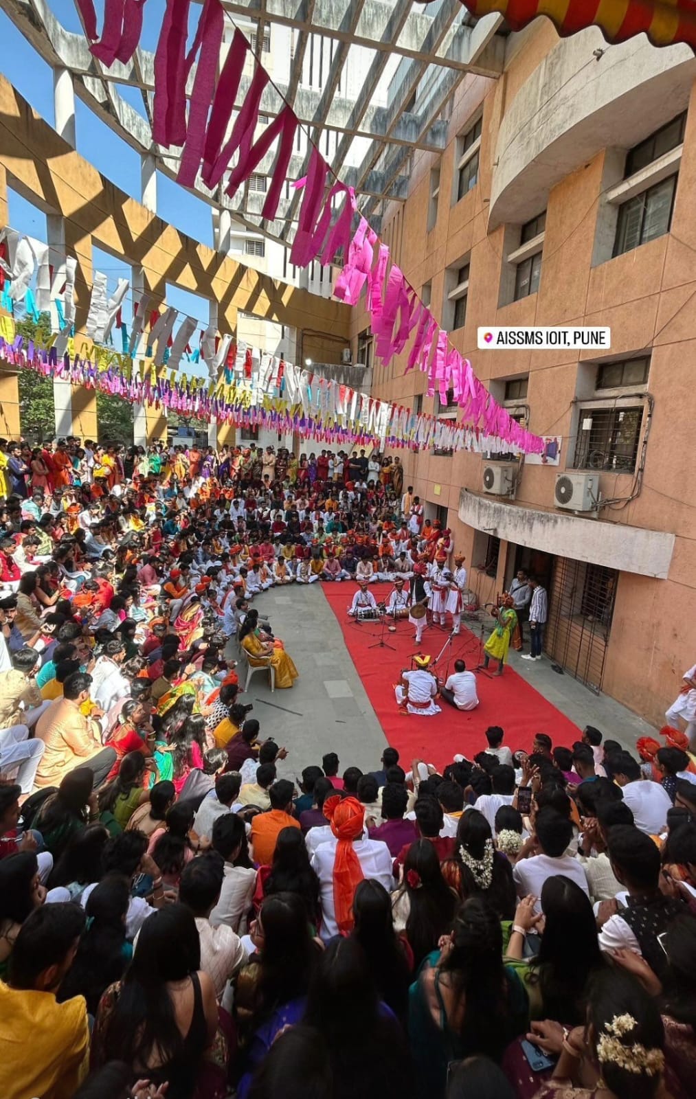 A crowded AISSMS IOIT courtyard decorated with colourful streamers during a performance.