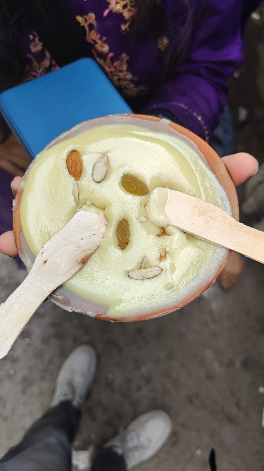 A clay bowl of pale yellow dessert topped with nuts and raisins, with two wooden spoons.