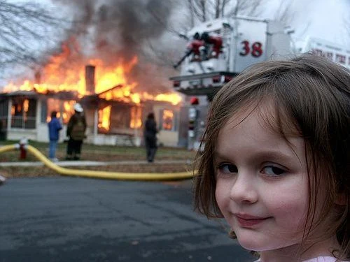Disaster Girl smiling at the camera while a house burns behind her.
