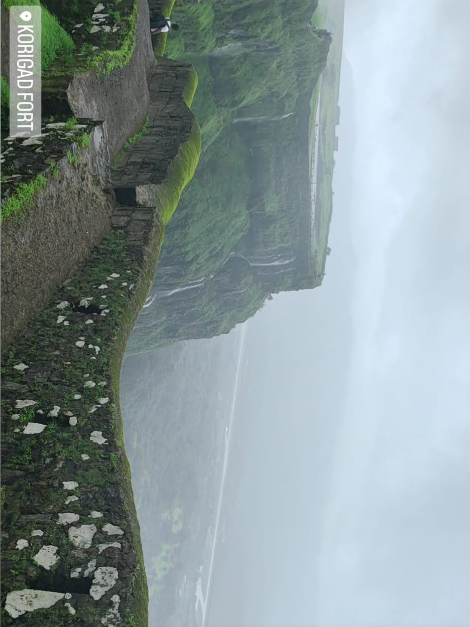 A photo of a stone path and fort walls above misty green hills, labelled Korigad Fort.