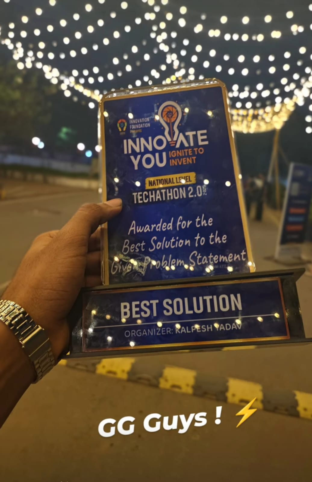 A hand holding a Techathon 2.0 Best Solution trophy beneath strings of lights, with the caption GG Guys!